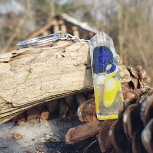 May include: A glass keychain with a blue and yellow design. The keychain is attached to a silver metal ring.