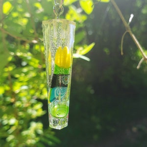 Puede incluir: Un llavero de resina transparente con una cadena plateada. La resina contiene formas abstractas de colores y una flor amarilla.