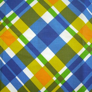May include: A close-up of a fabric with a plaid pattern. The design features intersecting diagonal lines in blue, green, yellow, orange, and white. The fabric has a slightly textured appearance, suggesting a woven material.