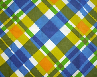 May include: A close-up of a fabric with a plaid pattern. The design features intersecting diagonal lines in blue, green, yellow, orange, and white. The fabric has a slightly textured appearance, suggesting a woven material.
