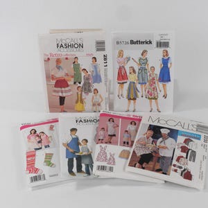 May include: A collection of six sewing pattern envelopes from McCall's and Butterick brands, featuring illustrations of aprons, socks, and uniforms. The white paper envelopes display various garment designs, model photos, brand logos, and product codes.