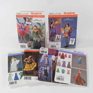 May include: A collection of six Simplicity sewing pattern envelopes featuring various costume and dress designs. The envelopes display photographic illustrations of models wearing finished garments, including fairy outfits, gowns, and dresses with diverse styles.