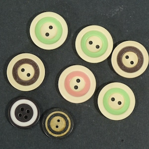 May include: Eight round buttons with different colored rings and two holes in the center. The buttons are in various colors, including brown, green, pink, and black.