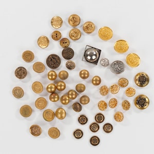 May include: A collection of vintage buttons in various sizes and designs. The buttons are primarily gold and bronze, with some silver and black accents. Styles include embossed, round, and spherical shapes, suitable for sewing or crafting projects.