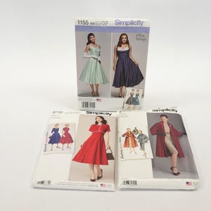 May include: Three Simplicity sewing patterns for dresses and a coat. The patterns are for vintage styles. The patterns are on white paper with black and white illustrations of the garments.