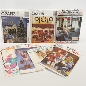 May include: A collection of eight vintage craft patterns for sewing and crafting projects. The patterns include a variety of themes, such as holiday decorations, pillows, and clothing. The patterns are in various colors, including red, blue, green, and white.