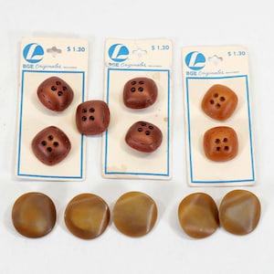 May include: Three sets of buttons in shades of brown. Two sets of square buttons are attached to vintage cards. The square buttons have four holes. The third set of buttons are round and have a marbled appearance.