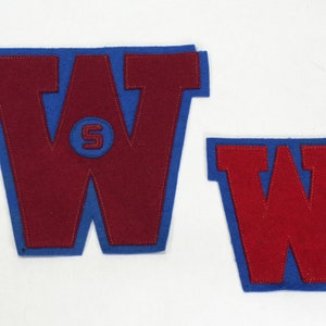 May include: Two felt patches in the shape of the letter W. The larger patch is blue with a red felt W inside. The smaller patch is blue with a red felt W inside. The larger patch has a smaller circle with the letter S inside.