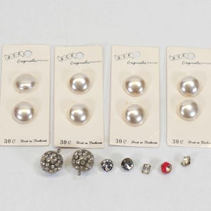 May include: A collection of vintage buttons, including four sets of large, pearlescent buttons on cards, and several smaller decorative buttons. The cards read "B-G-E Originales" and "30¢ First in Fashions".