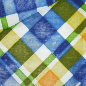 May include: Close-up of a fabric with a plaid pattern. The design features a mix of blue, green, yellow, and orange squares, creating a colorful and textured appearance. The fabric is folded, showing the pattern's continuity.