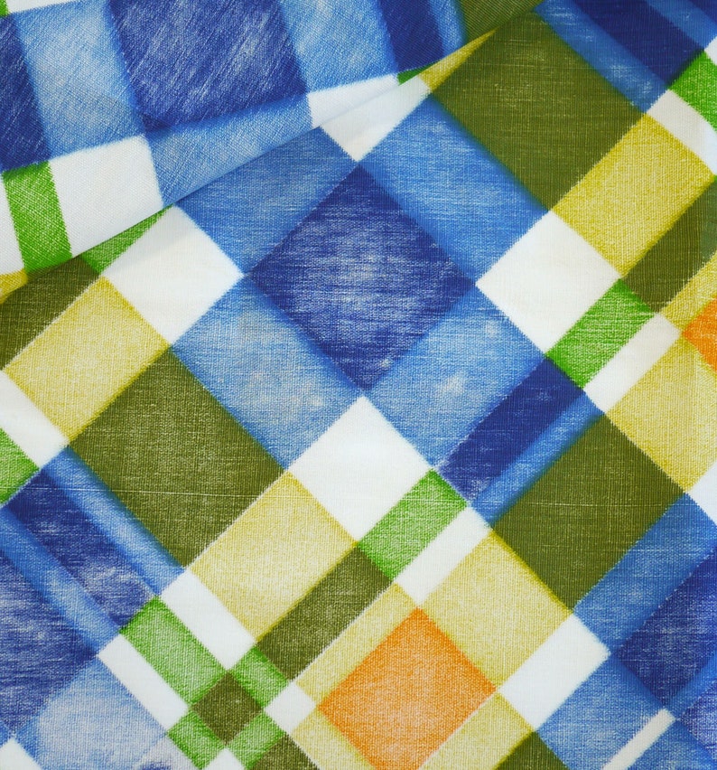 May include: Close-up of a fabric with a plaid pattern. The design features a mix of blue, green, yellow, and orange squares, creating a colorful and textured appearance. The fabric is folded, showing the pattern's continuity.