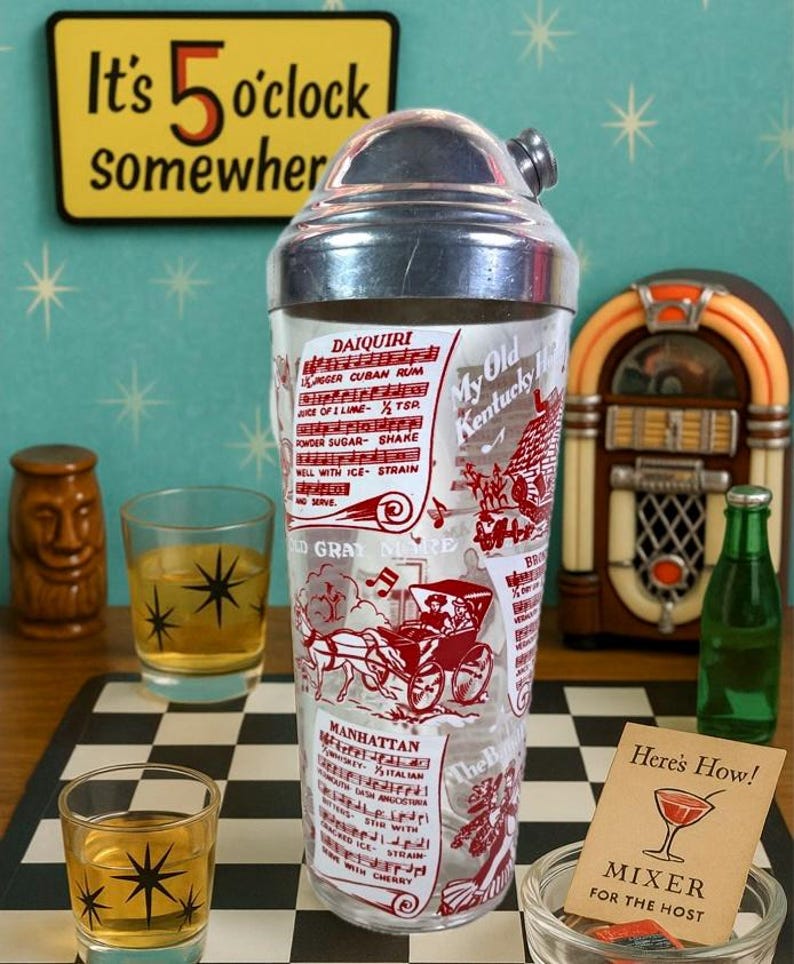 Puede incluir: Una coctelera vintage con tapa plateada y cuerpo de vidrio transparente, con recetas de c&oacute;cteles e ilustraciones impresas en rojo. La imagen incluye un letrero que dice "It's 5 o'clock somewhere" y una peque&ntilde;a tarjeta que dice "Mixer for the Host".