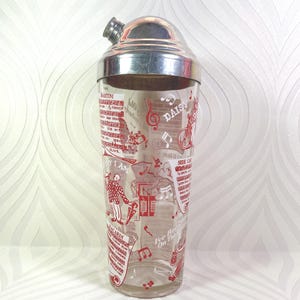 Puede incluir: Una coctelera vintage con tapa plateada y cuerpo de vidrio transparente. El vidrio est&aacute; decorado con ilustraciones rojas de notas musicales, recetas de c&oacute;cteles y las palabras "MARTINI", "DAISY" y "BACARDI".