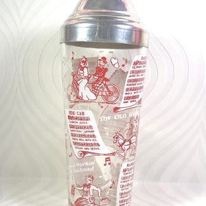 Puede incluir: Coctelera vintage con tapa plateada y cuerpo de vidrio transparente. El vidrio est&aacute; decorado con ilustraciones rojas de personas, notas musicales y recetas de c&oacute;cteles. El texto incluye "Side Car" y "The Old Grand".
