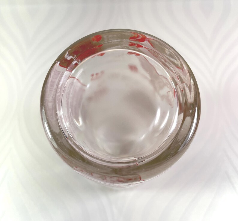 Puede incluir: Un cenicero de vidrio transparente con forma redondeada. El borde del cenicero tiene dise&ntilde;os florales rojos. El cenicero est&aacute; vac&iacute;o y se encuentra sobre una superficie blanca con un patr&oacute;n sutil.