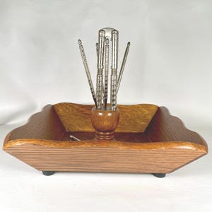 May include: A vintage nutcracker set featuring a wooden tray with a scalloped edge and a central wooden holder for the nutcrackers. The set includes several silver-toned nutcrackers and picks, perfect for serving nuts.