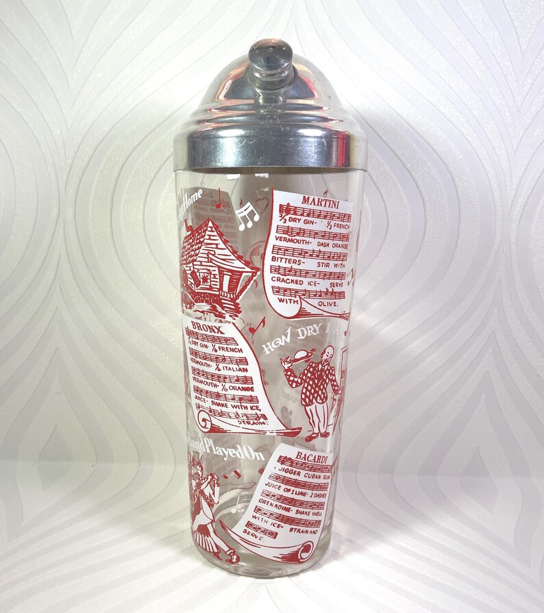 Puede incluir: Coctelera vintage con tapa de acero inoxidable y cuerpo de vidrio transparente. El vidrio est&aacute; decorado con ilustraciones y texto en rojo, incluidas recetas de c&oacute;cteles. La coctelera est&aacute; dise&ntilde;ada para mezclar bebidas.