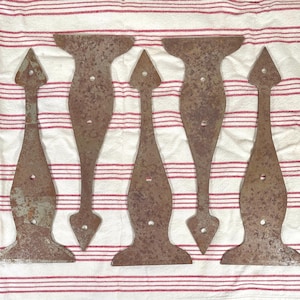 May include: Five matching metal strap hinges with a weathered, rusted brown finish. Each hinge features a pointed spear-shaped tip at the top, a wide base at the bottom, and a central body with pre-drilled circular holes for mounting hardware.