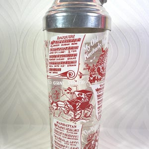 Puede incluir: Coctelera vintage con tapa de acero inoxidable y cuerpo de vidrio transparente. El vidrio est&aacute; decorado con ilustraciones y texto en rojo, incluidas recetas de c&oacute;cteles como Daiquiri y Manhattan.