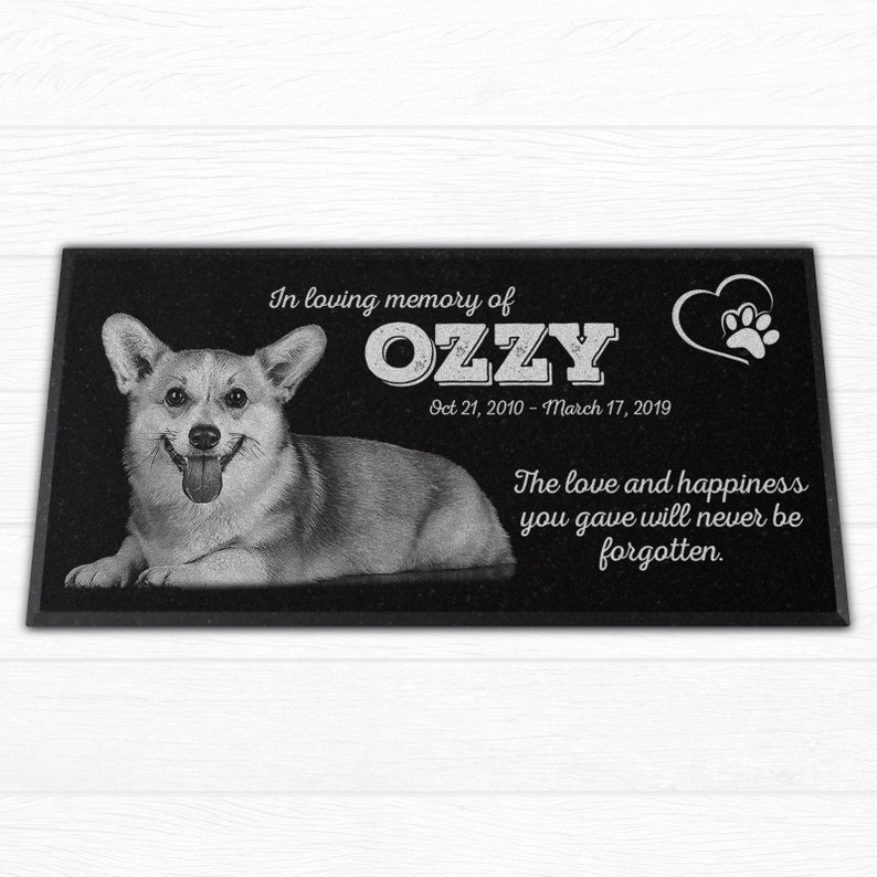 May include: Black granite memorial stone with a photo of a corgi dog, the name "OZZY" in white lettering, and the dates "Oct 21, 2010 - March 17, 2019". The text "In loving memory of" and "The love and happiness you gave will never be forgotten." is also included.