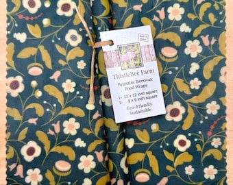 May include: Reusable beeswax food wraps from ThistleBee Farm. The wraps feature a dark teal floral pattern with white and gold accents. Includes one 12 x 12 inch square and one 9 x 9 inch square wrap. Eco-friendly and sustainable.