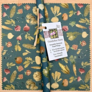 May include: Reusable beeswax food wraps from ThistleBee Farm. The wraps are teal with a vegetable pattern and come in 12 x 12 inch and 9 x 9 inch squares. A rolled wrap is tied with twine.