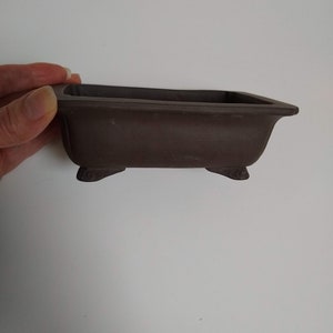 May include: A dark brown rectangular bonsai pot with three small feet on the bottom.
