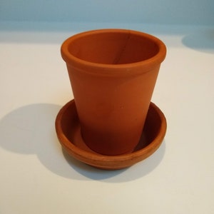 May include: A small terracotta pot with a matching saucer. The pot is empty and ready for planting.