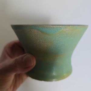May include: A green ceramic bowl with a textured surface. The bowl has a wide rim and a rounded bottom.