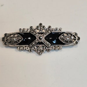 May include: A silver brooch with black enamel and marcasite stones in a geometric design.