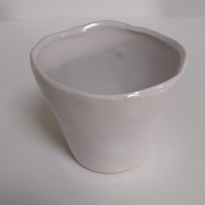 May include: A white ceramic planter with a wavy rim. The planter is empty and has a smooth, matte finish.