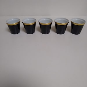 May include: Five black espresso cups with a gold rim. The cups are lined up in a row on a white surface.