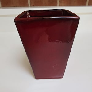 May include: A deep red ceramic planter with a square shape and a glossy finish.
