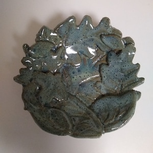 May include: A ceramic dish with a blue-green glaze and a design of leaves. The dish is handmade and has a rustic look.