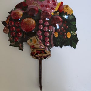 May include: A decorative metal hook shaped like a fruit basket with painted grapes, apples, and leaves. The hook is brown and has a rustic look.