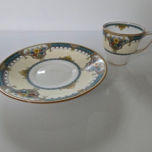 May include: A white teacup and saucer with a gold rim and a floral design in shades of blue, yellow, and green.
