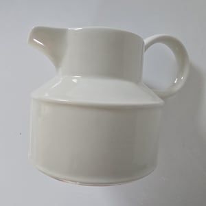 May include: A white ceramic pitcher with a spout and a rounded handle. The pitcher has a cylindrical base and a slightly flared top. The overall design is simple and elegant, suitable for serving beverages.