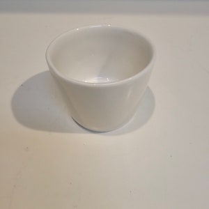 May include: A white ceramic cup with a rounded bottom and a wide opening.