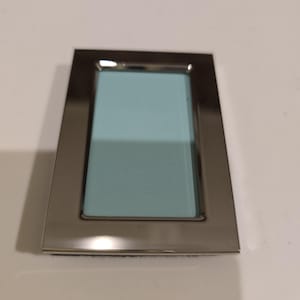 May include: A rectangular silver-toned picture frame with a light blue interior. The frame has a simple, modern design with a polished finish. The frame is designed to hold a photograph or artwork.