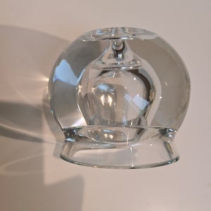 May include: A clear glass bottle stopper with a round base and a smaller, round, hollowed-out top.