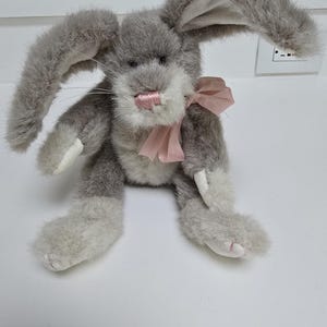 May include: A plush gray bunny with long, floppy ears and a pink bow. The bunny has white accents on its paws and inner ears, and a pink nose. The toy is soft and fluffy, perfect for a child's room or Easter decor.
