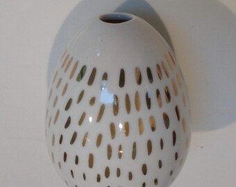 May include: White ceramic vase with a round shape and gold speckles.