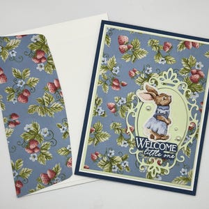 Petit lapin de bienvenue dans un livre d'histoires dans un cadre fleuri. Blanc à l'intérieur pour un message personnel. Carte de félicitations pour bébé.