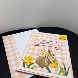 Ostergruß. Hintergrund rosa-weiß kariert. Häschen, Küken und Narzissen. Innerhalb Sentiment-"Ein Häschen liebt dich" und Häschen.
