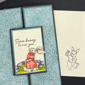 Pop up Klappkarte Häschen mit Bilderbuch. Türkis, Koralle und Dunkelbraun. Sentiment „Some Bunny Loves You“ Passender Umschlag mit Hasenmotiv.