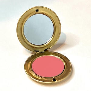 Peut inclure: Un blush compact dans un boîtier doré avec un miroir. Le blush est de couleur rose clair.