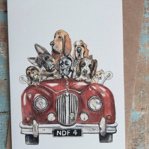 May include: A watercolor greeting card featuring a red vintage car filled with various dog breeds. The dogs are of different sizes and colors, with some looking over the car's windshield. The license plate reads "NDF 4".