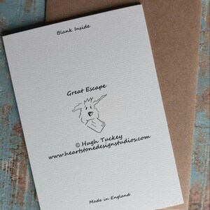 May include: A white card with black text that reads "Blank Inside", "Great Escape", "&copy; Hugh Tuckey", "www.heartstonedesignstudios.com", and "Made in England". The card features a cartoon illustration of a dog with a letter in its mouth.