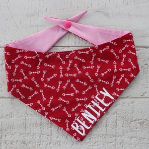 May include: Red and pink dog bandana with a white arrow and heart pattern and the name "BENTLEY" printed in white.
