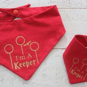 May include: Two red dog bandanas with gold glitter text and images. The larger bandana says "I'm a Keeper" with three golden snitch images. The smaller bandana says "I'm a Keeper" with two golden snitch images.